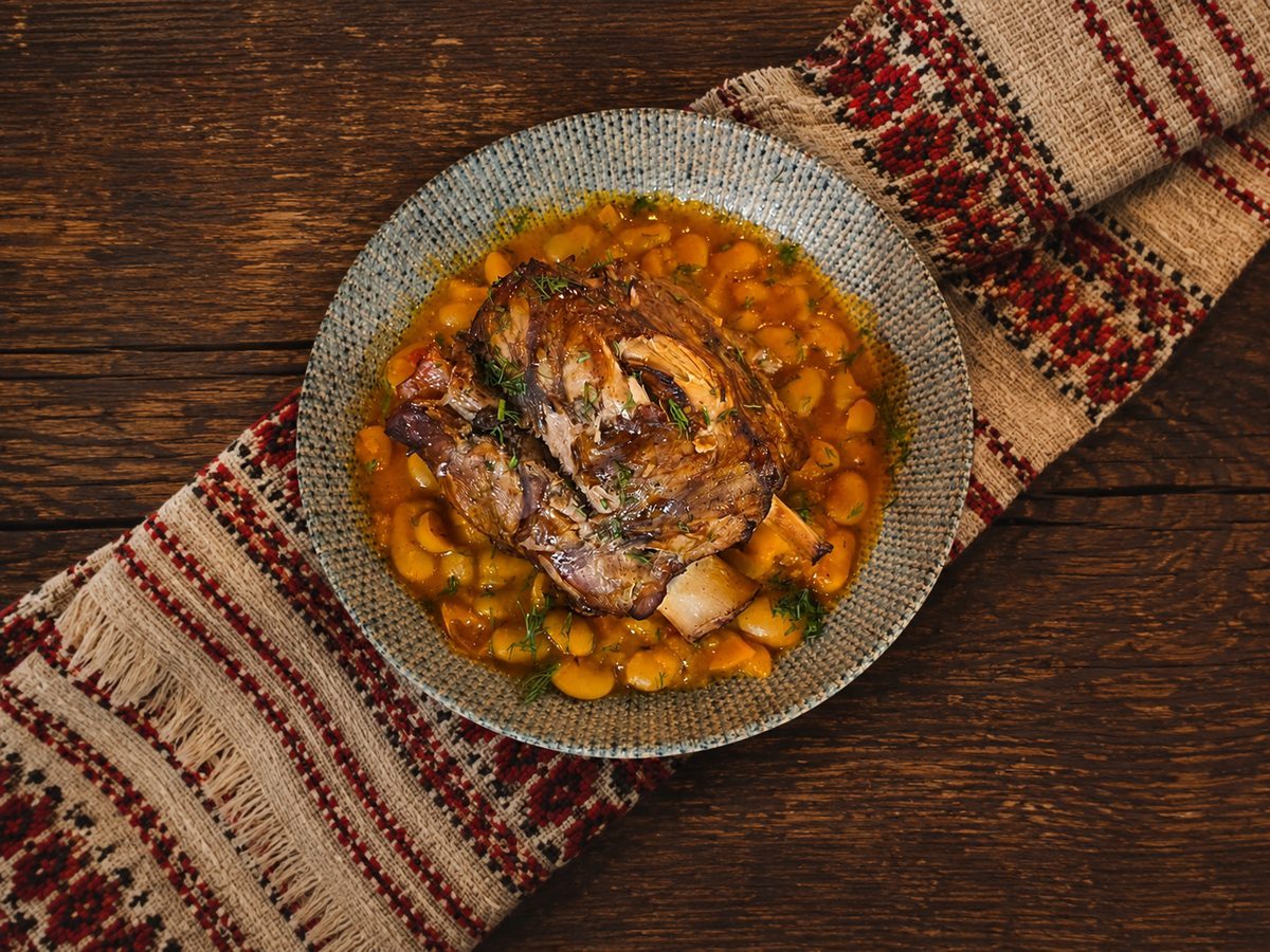 Pork knuckle with beans on a ceramic plate, on a wooden table with a cloth, at Restaurant Ceaun